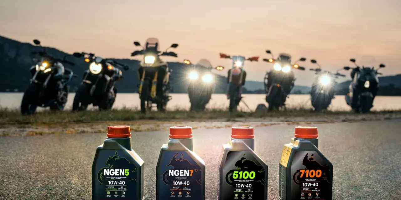 Cztery butelki oleju Motul do motocykla: NGEN5, NGEN7, 5100 i 7100, stoją na drodze o zachodzie słońca, za nimi widać rzędem motocykle.