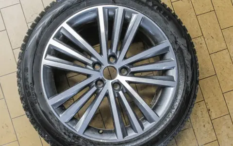 Felga aluminiowa z oponą zimową na tle kafelków.