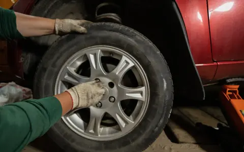 Ręce w rękawiczkach przykręcają śruby koła. Zastanawiasz się, ile kosztuje wymiana opon z wyważeniem?