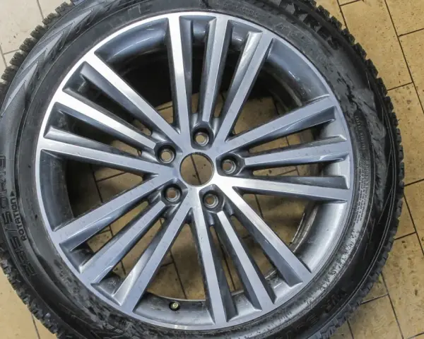Felga aluminiowa z oponą zimową na tle kafelków.